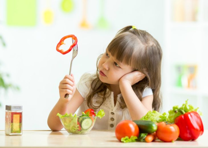 Cute kid girl not wanting to eat healthy food at kitchen